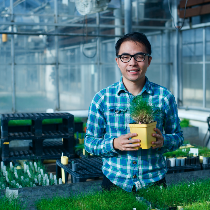 Yinjie Qiu in the greenhouse holding a planter with turfgrass