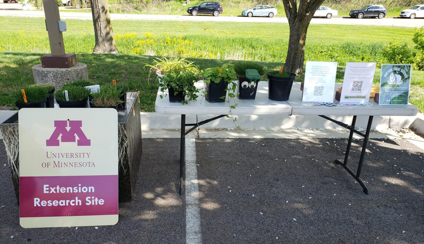 a table set up outside for an event with plant specimen and University of Minnesota signs
