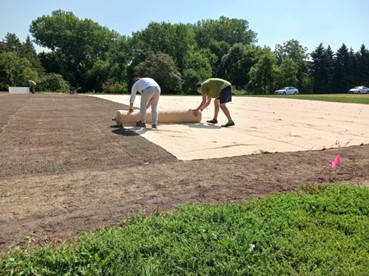 two people laying out a roll of seeding blanket