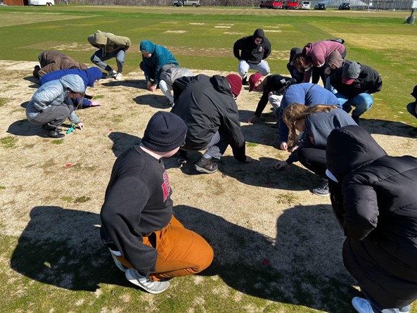 a group of students outside closely examining a patch of dead grass at a turfgrass