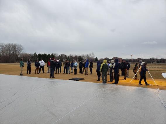 a group of people gathered around turfgrass research plots in late winter